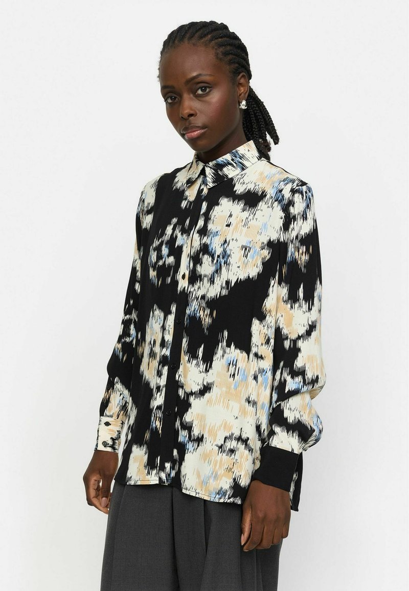 Lange mouw blouse in zwart, crème en lichtblauw abstract patroon. Gemaakt van een gladde stof met een knoopsluiting aan de voorkant en een standaard kraag.