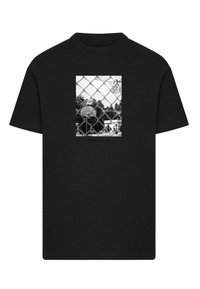 Camiseta de algodón negra con un gráfico rectangular de una cancha de baloncesto cercada, con un aro grande y árboles, el texto dice "NO SOLO UN JUEGO".