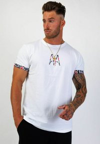 Vit kortärmad T-shirt med blomstermönstrad kant på ärmarna och fet broderad text på bröstet.