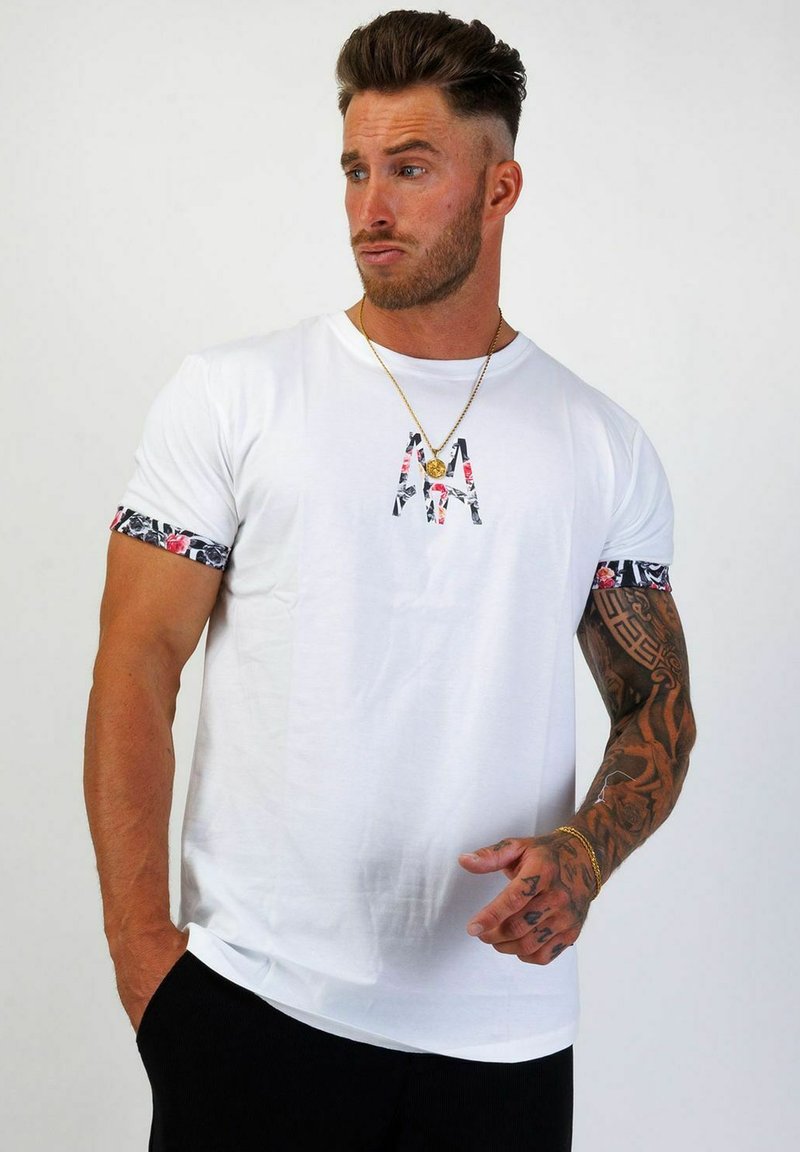 Vit kortärmad T-shirt med blomstermönstrad kant på ärmarna och fet broderad text på bröstet.