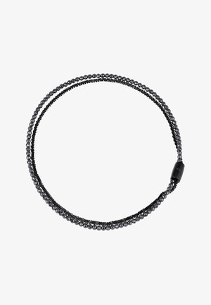 Mustavalmoinen joustava hiusnauha, jossa on pieniä kiiltäviä helmiä ja saumaton sylinterimäinen suljin valkoisella taustalla.