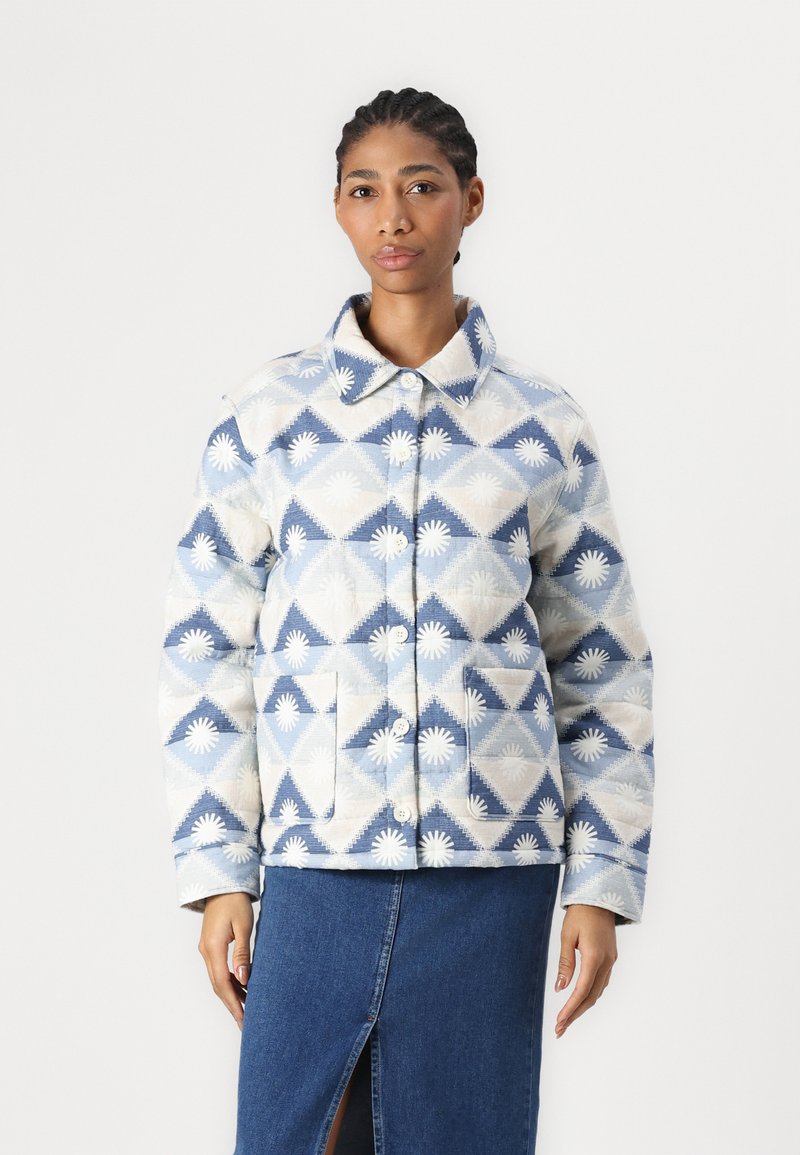 Chaqueta acolchada con un patrón geométrico en azul y blanco, que cuenta con un cuello extendido, botones en el frente y dos bolsillos de parche en la parte delantera.