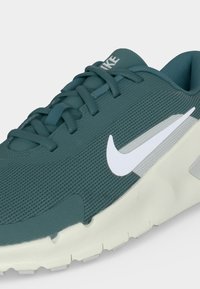 Γαλάζιο πλεκτό αθλητικό παπούτσι Nike με λευκό λογότυπο Swoosh, γαλάζια κορδόνια και χοντρή υπόλευκη σόλα, σε κοντινή προβολή από το πλάι.