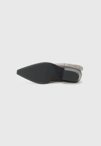 Bota de cuero a la altura del tobillo con punta afilada, parte superior texturizada en gris y suela de goma negra, con estrías para mayor tracción.