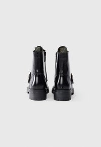 Black leather ankle boots with a glossy finish, featuring a side zip, textured accents, and a thick, rugged sole.