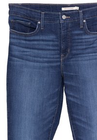 Jeans skinny de denim azul oscuro con cintura alta, cinco bolsillos y costuras en contraste. Cuenta con cremallera y cierre de botón.