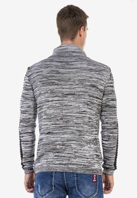 Grau- und schwarz gestreifter Pullover mit hohem Kragen und langen Ärmeln, der ein strukturiertes Strickmuster und kontrastierende schwarze Akzente entlang der Ärmel aufweist.