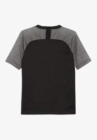 Camiseta deportiva negra con un panel texturizado gris y un patrón brillante en la parte posterior, y un cuello corto con un lazo para colgar.