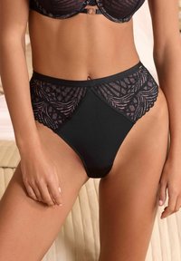 Slips neri a vita alta con un design in pizzo, bordi smerlati e una vita liscia. Il tessuto ha una finitura lucida con motivi intricati.