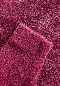 Tapis pelucheux de couleur magenta vif avec une texture dense et scintillante. La surface présente de longues fibres douces et des variations de couleur subtiles.