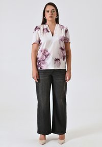 Blusa bianca con stampa floreale viola, scollatura a V, maniche corte; abbinata a pantaloni jeans a gamba larga scuri e scarpe con tacco nude.