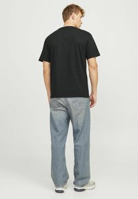 Sort bomulds T-shirt med korte ærmer, afslappet pasform og rund hals. Båret med lyseblå denim jeans og sporty sko.