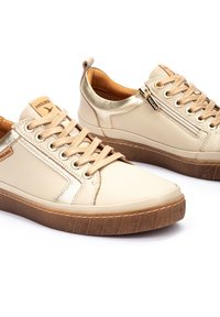 Beige lederen sneakers met gouden accenten, ronde neus, platte rubberen zool en vetersluiting. Inclusief zijrits en tekstuurdetail op de zool.