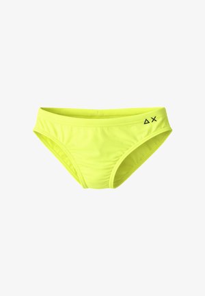 Costume da bagno slip giallo brillante con un piccolo logo nero Delta e X sulla parte anteriore destra della cintura, su sfondo bianco.