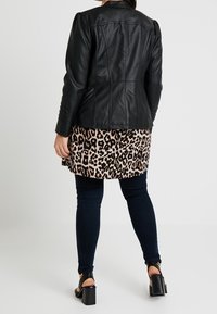 Zwarte leren jas met een getailleerd ontwerp en accenten op de schouders, gecombineerd met een jurk in luipaardprint, donkere jeans en zwart blokhakken sandalen.