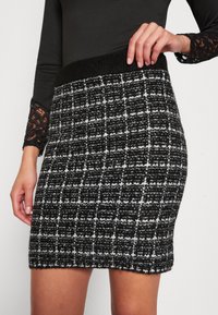 Mini sukně s černobílým kostkovaným vzorem vyrobená z texturované tkaniny, se širokým pasem a přiléhavým střihem.