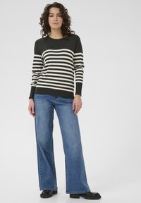 Pull rayé noir et blanc à manches longues, associé à un jean bleu clair à jambes larges et des bottes noires. Design simple et décontracté.