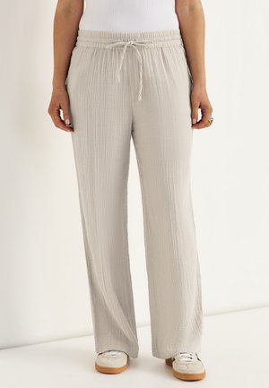 Lichtbeige broek met brede pijpen en een taille met trekkoord, gedragen met witte sneakers en een wit mouwloos topje.