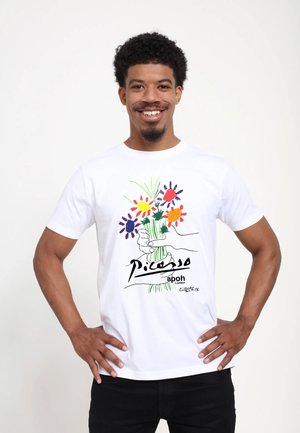 Bílý tričko s motivem ruky držící kytici s barevnými květinami. Design obsahuje nápisy "Picasso" a "apoh London" ve výtvarné typografii.