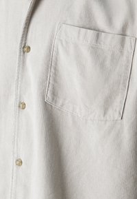 Helles beige Cordhemd mit einer kleinen Brusttasche, sechs Knöpfen und vertikaler Rippstruktur.