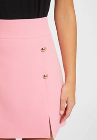 Gonna rosa con vita alta, caratterizzata da uno spacco laterale e due bottoni dorati sulla parte frontale. Tessuto dalla texture liscia.