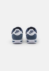 Mornarice plave tenisice od suede i mrežastog materijala, s bijelim detaljima i izraženim oblikom potpetice, na kojoj se nalazi Nike logo.