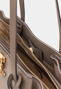 Graue Lederhandtasche mit goldfarbenen Beschlägen, zeigt Reißverschlussfächer und ein strukturiertes Innenfutter. Verfügt über zwei Griffe und ein strukturiertes Design.