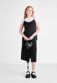 Musta midi-mekko valkoisen T-paidan päällä, jossa on pitsikoristeita. Sydämen muotoinen musta käsilaukku ja massiiviset mustat kengät täydentävät asun.