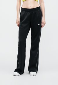 Pantaloni sportivi negri dintr-un material neted, cu o croială confortabilă, talie elastică, dungi albe pe lateral și logo-ul Nike în față.