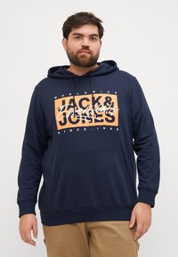 Granatowa bluza z kapturem, z przednią kieszenią, sznurkami i graficznym napisem w kolorze pomarańczowym i białym. Miękki materiał, luźny krój, casualowy styl.