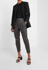 Zwarte op maat gemaakte blazer, fitted zwart top en grijze leren broek met een gladde textuur. Zwarte block-heeled sandalen maken het ensemble compleet.