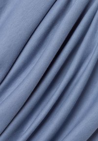 Miękka, jasnoniebieska tkanina o gładkich, ukośnych fałdach i delikatnej fakturze ukazującej drobny wzór dzianiny.