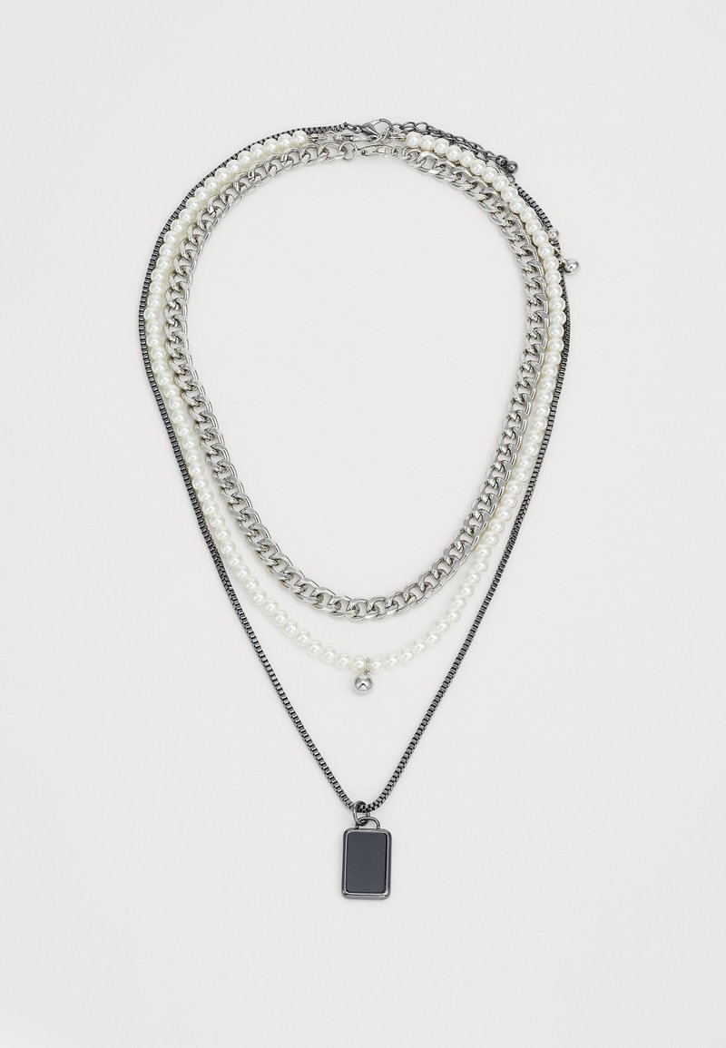 Colar em camadas com corrente de prata, pérolas brancas e um pendente retangular preto. Combina várias texturas e formas.
