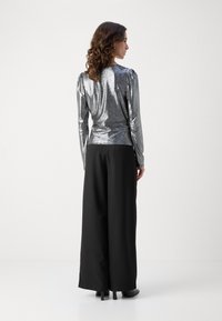 Sjajni srebrni long-sleeve top s nabranim ramenima, uparen s crnim hlačama širokih nogavica, koje imaju glatku teksturu i elegantan dizajn.