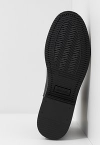 Suela de zapato de goma negra con un patrón de espiga, marca en relieve "ANNA FIELD" y una textura suave en la sección superior.