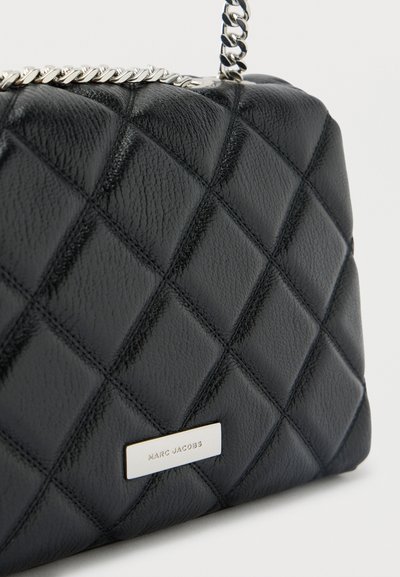 Μαύρη τσάντα ώμου από καπιτονέ δέρμα με αλυσίδα ασημί λουρί και ορθογώνια μεταλλική ετικέτα με ανάγλυφη την επιγραφή «Marc Jacobs» στο μπροστινό μέρος.