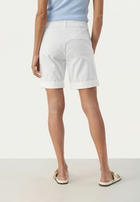 Pantaloni corti bianchi in cotone con risvolti, progettati con una vita piatta e due tasche posteriori a toppa. Modello con sandali beige.