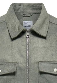 Green, textured jacket with a spread collar, front zipper, and buttoned chest pockets. Features a subtle patterned fabric.