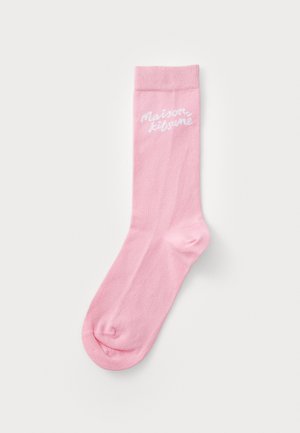 Calzino di cotone rosa con bordo a costine e superficie liscia. Presenta un logo ricamato bianco "maison kitsuné" vicino alla parte superiore.