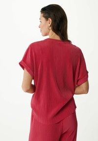 Červený žebrovaný top s krátkými ohrnutými rukávy a volnějším střihem, s jemnou texturou a zaobleným spodním lemem.