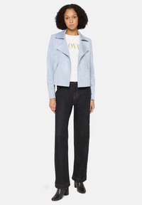 Jasnoniebieska kurtka motocyklowa z imitacji zamszu o krótkim kroju, z zamykanymi na zamek kieszeniami i szpiczastymi klapami, zestawiona z wysokim stanem czarnych dżinsów.