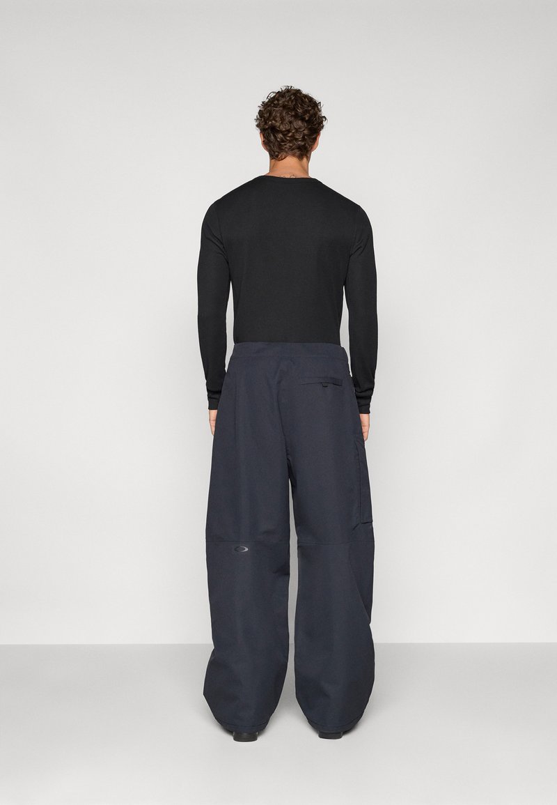 Black long-sleeve shirt paired with oversized navy blue pants. Pants feature a logo on the leg and a side pocket. Smooth fabric texture.