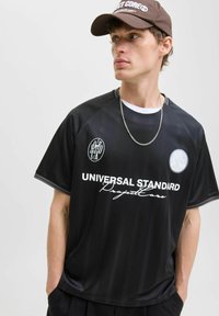 Maillot de sport noir avec des rayures verticales, portant "UNIVERSAL STANDARD" en texte blanc, logos ronds et manches courtes.