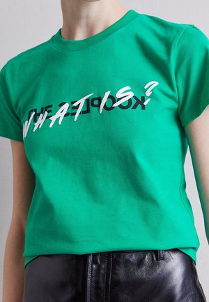 Person wearing a green t-shirt with layered text designs reading “What is?” and “The Exceptions?” paired with black leather pants.