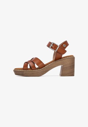 Sandalia de tacón marrón de cuero con tiras entrecruzadas, hebilla en el tobillo y plataforma con textura de madera. Tacón grueso y resistente con detalle de costuras.