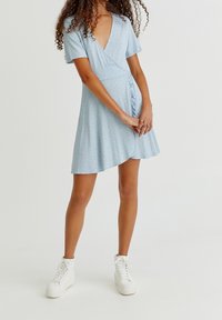 Vestido corto de manga corta en azul claro con patrón floral, escote en forma de V y detalle fruncido en el lateral. Combinado con zapatillas altas blancas.