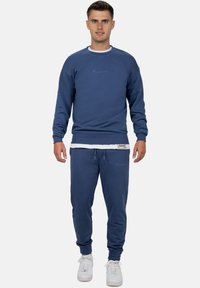 Felpa blu e pantaloni coordinati in tessuto morbido. Presenta polsini e vita a coste, con un logo ricamato in blu più chiaro.