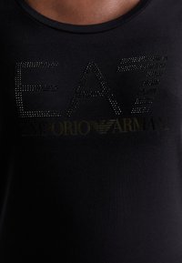 Melnas kokvilnas t-kreklas ar rhinestone rotājumiem, kas veido vārdu "EAT" un "Emporio Armani", ar apaļu kakla izgriezumu un mīkstu tekstūru.