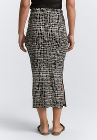 Jupe crayon en noir et blanc à motif, avec une fente sur le côté, fabriquée en tissu extensible, dotée d'un design ajusté et d'une texture lisse.