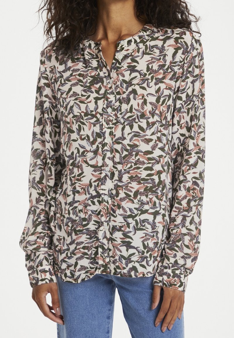 Blusa a maniche lunghe con motivo a foglie nei toni del verde, rosa e blu. Presenta una chiusura con bottoni davanti e un collo rotondo, realizzata in un tessuto leggero.